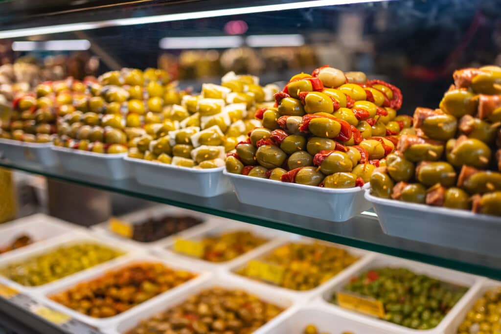 Counter of a market with piles of food, olives and pickles in a colorful exhibition, Mercado San Miguel, Madrid.