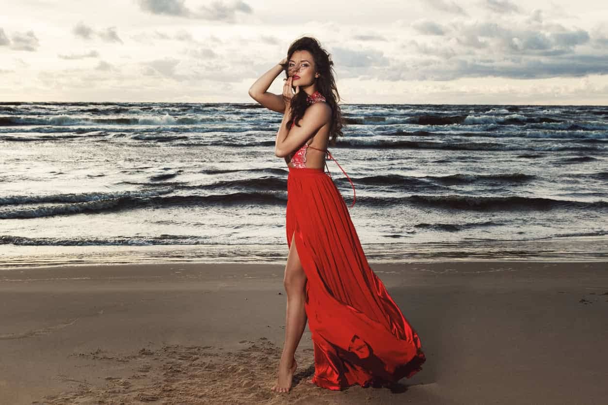 Stunning woman wearing beautiful red dress on the beach during sunset time - What to wear to a wedding in Ibiza.