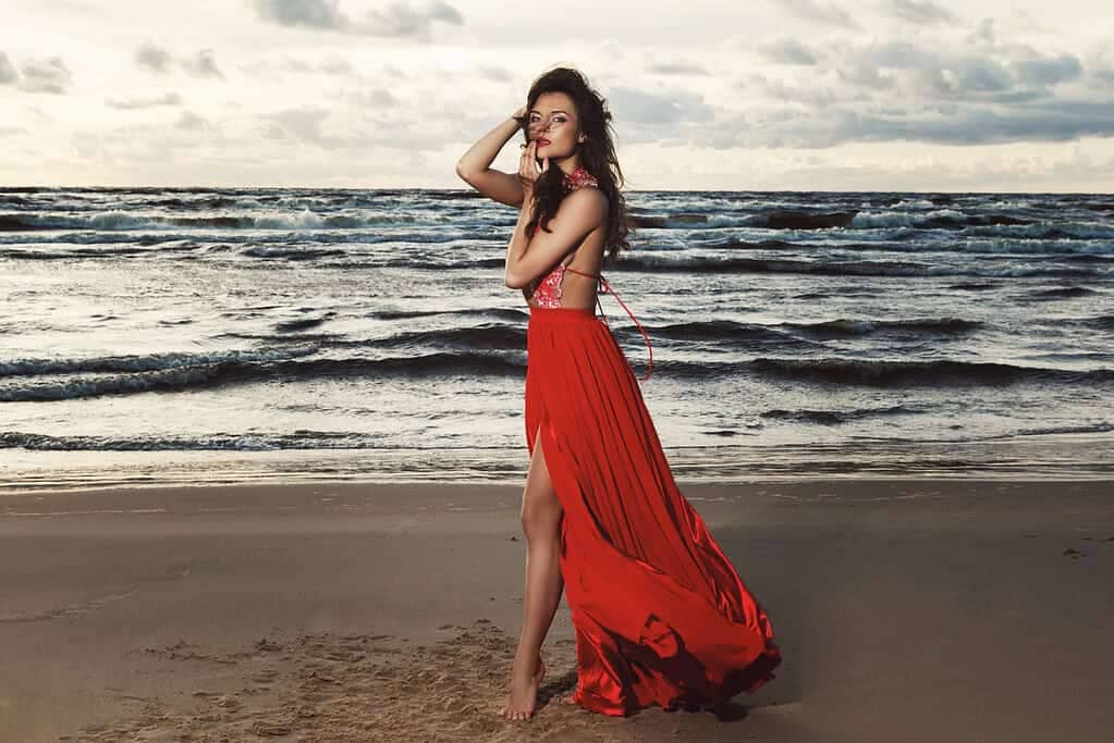 Stunning woman wearing beautiful red dress on the beach during sunset time - What to wear to a wedding in Ibiza.